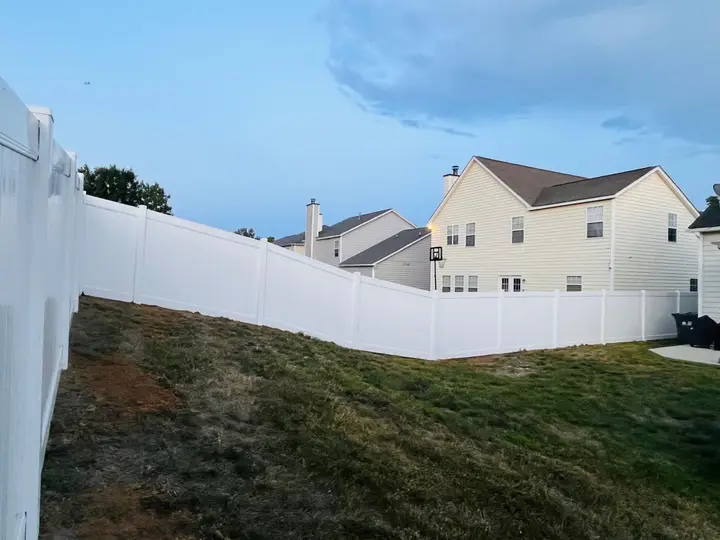 White vinyl privacy fence running along a backyard lawn